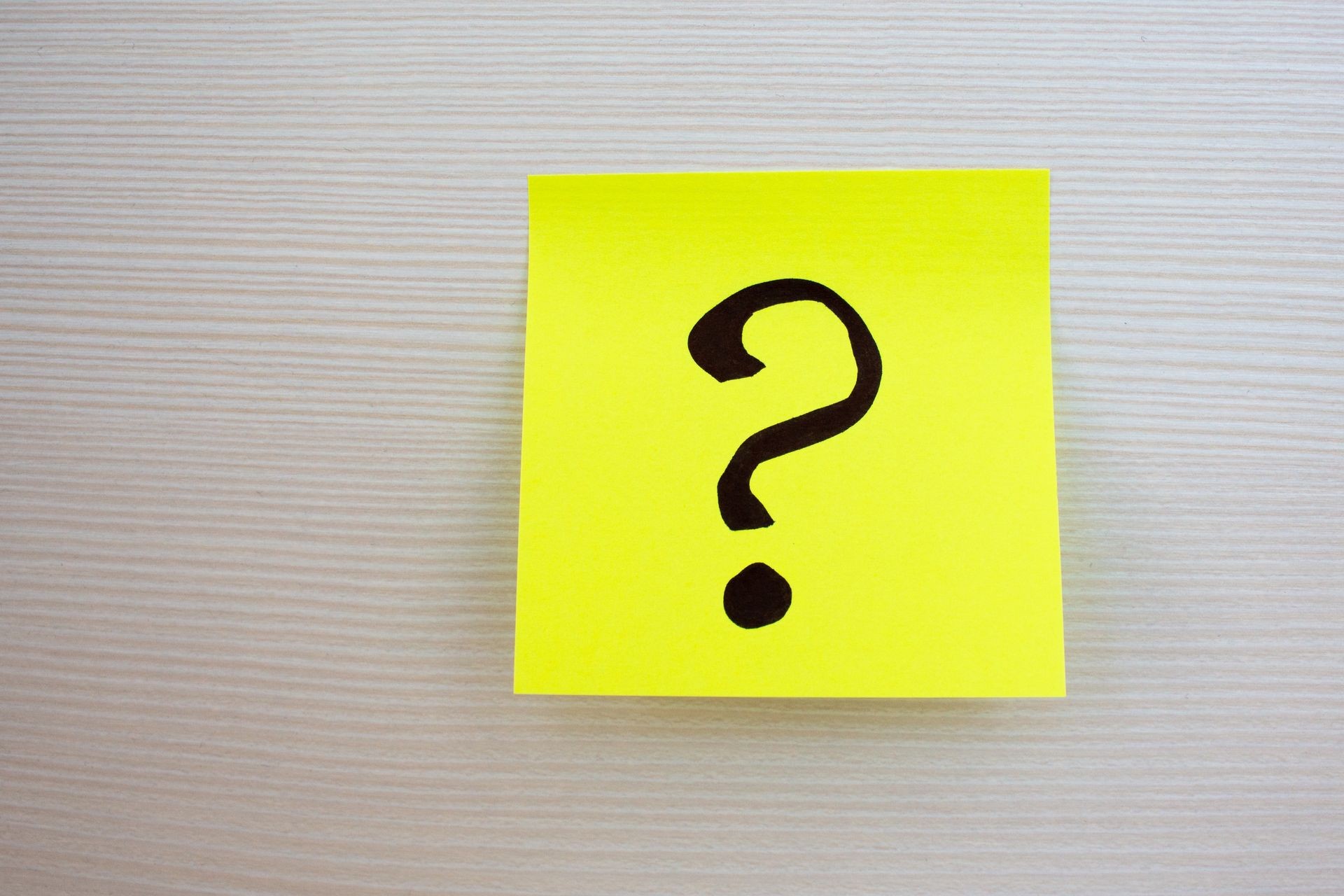 Question mark on a yellow sticker on a wooden background